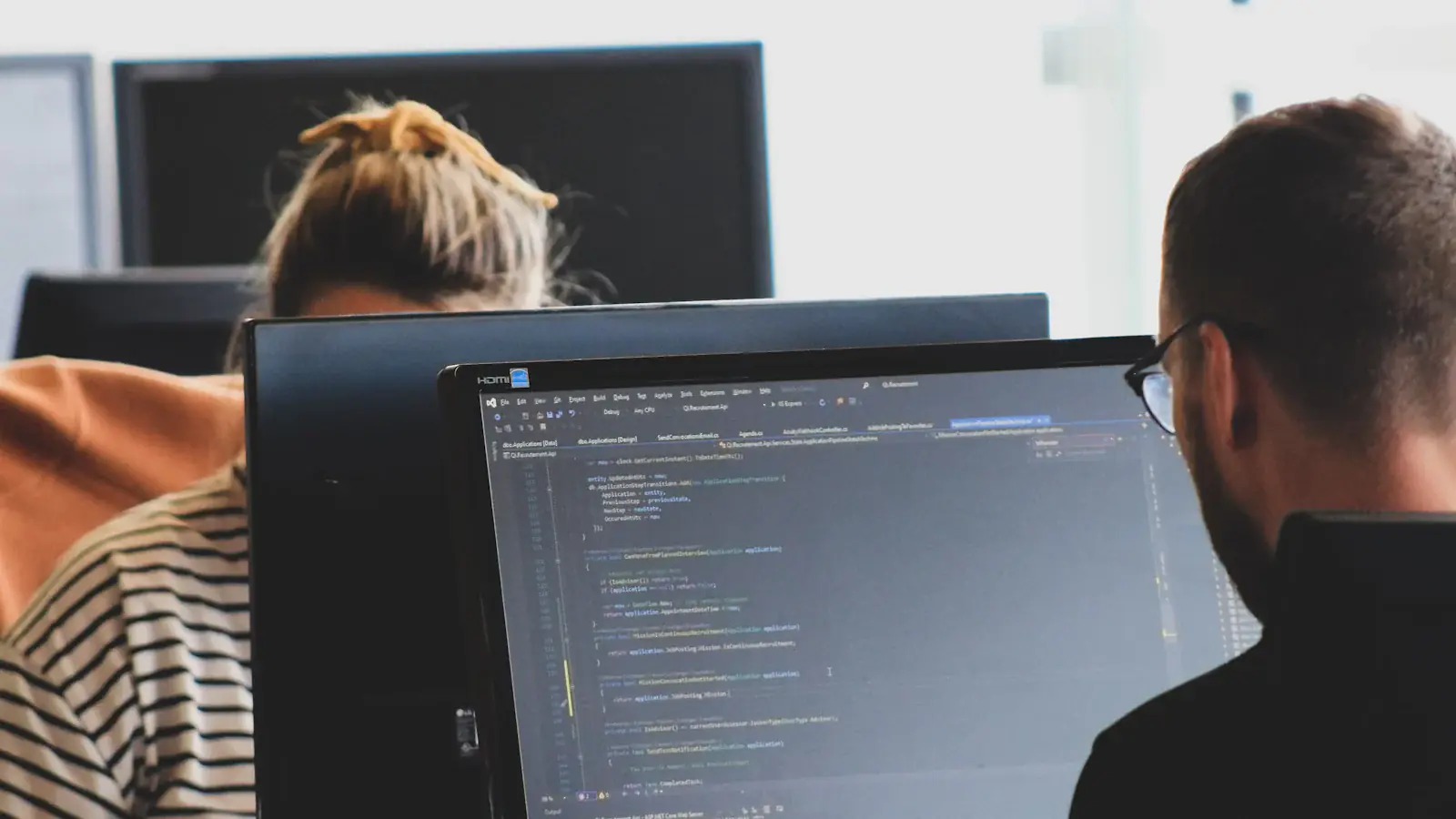 Two developers working on code at their monitors in a bright office